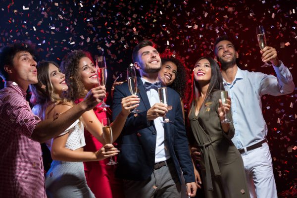 Diverse people celebrating New Year at nightclub, holding champagne flutes and looking upwards